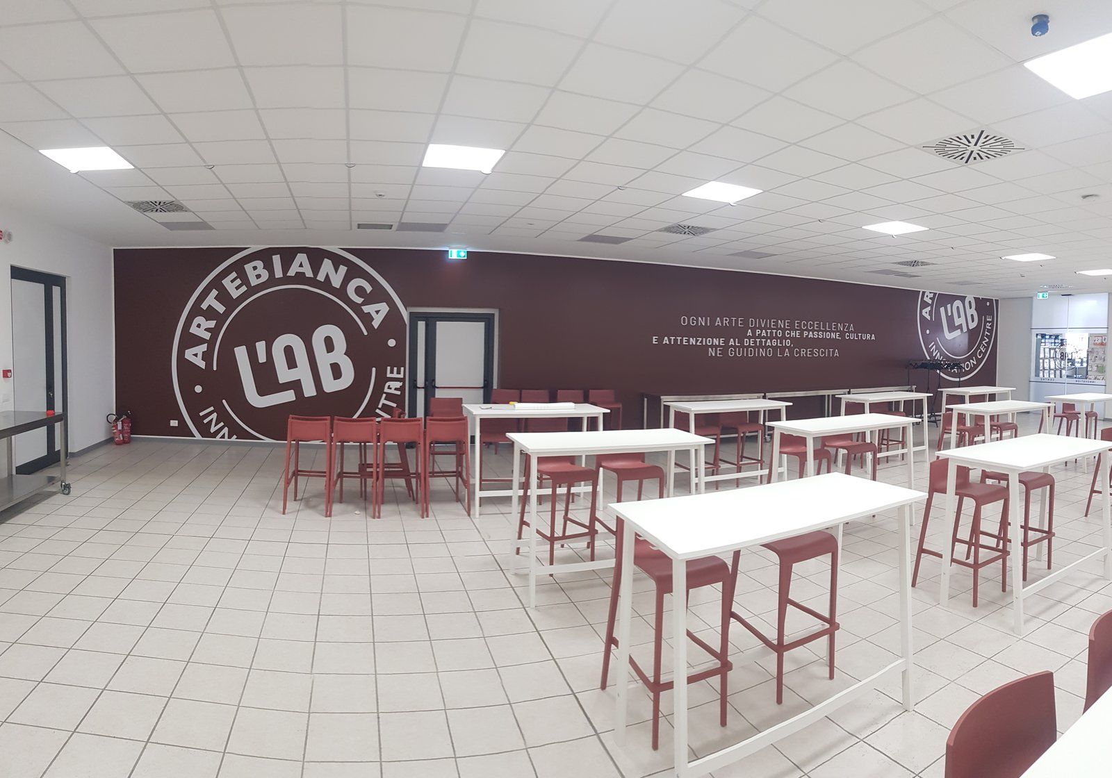 Grande parete bordeaux con logo Artebianca e lettering in una sala con tavoli alti