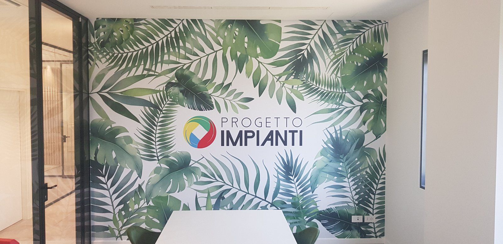 Parete d’ufficio con rivestimento a foglie tropicali e logo Progetto Impianti