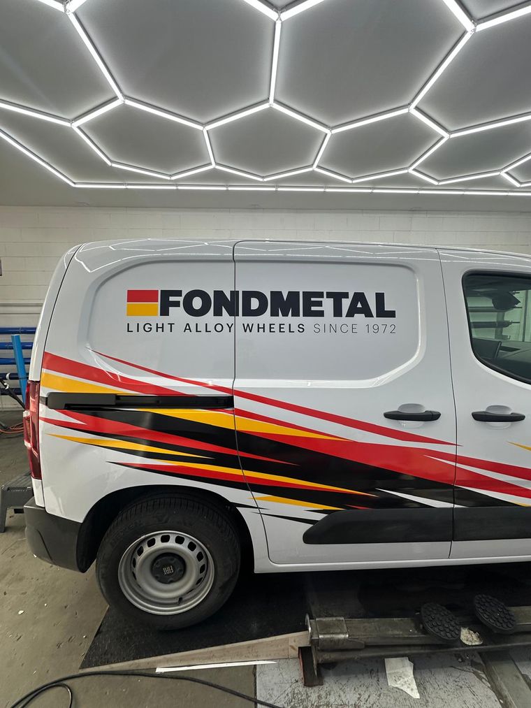 Fiancata di un furgone bianco Fondmetal con logo e fasce grafiche rosse, gialle e nere, in sala wrapping