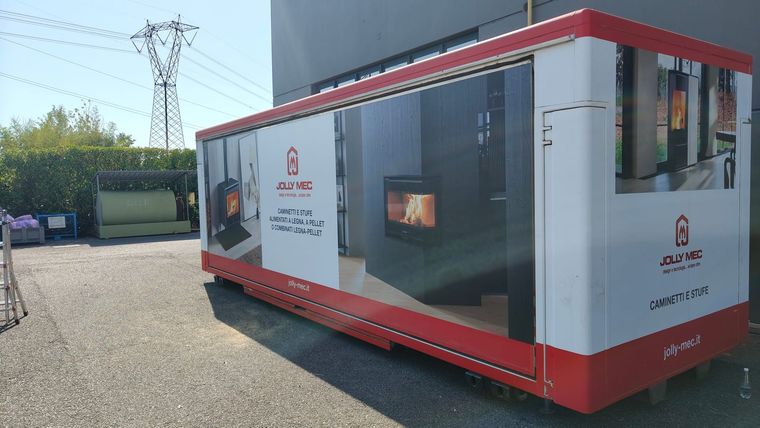 Container espositivo bianco e rosso Jolly Mec con pannelli stampati di stufe e caminetti, in piazzale