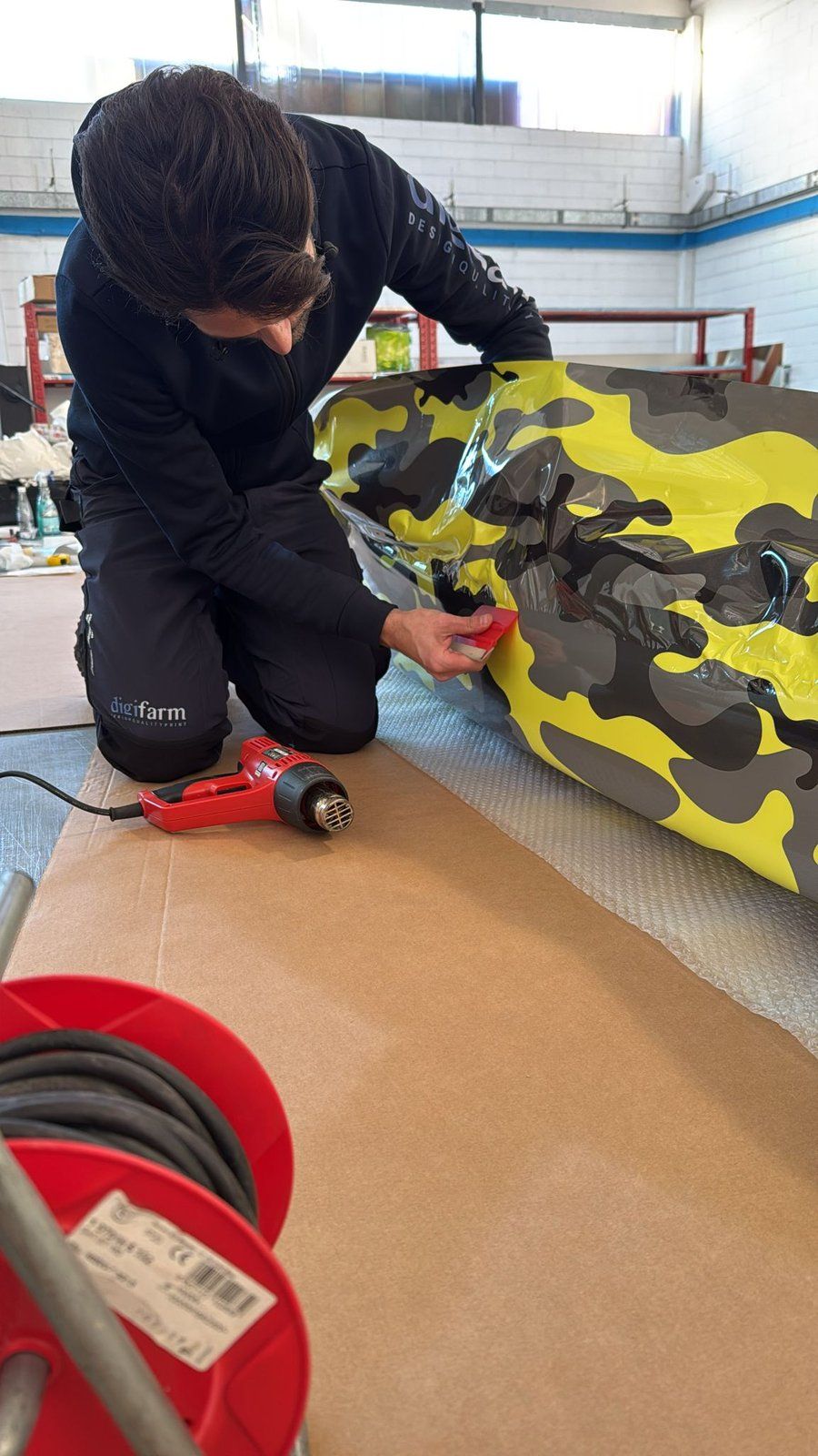 Tecnico applica pellicola camouflage giallo-nera sullo scafo di una barca